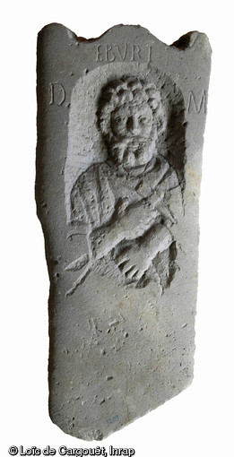 Stèle funéraire gallo-romaine en grès (hauteur 93 cm, largeur 38 cm), première moitié du IIe s. de notre ère, nécropole de Pont-l'Évêque, Autun (Saône-et-Loire), 2004.  Le seul attribut observable ici est un marteau mince à panne pointue : le défunt était sans doute sculpteur de pierre ou dinandier. La surface de la stèle a été polie avec soin, seule l'inscription se détache :  Eburi D(iis) M(anibus) ,  Aux dieux Mânes d’Eburus . 
