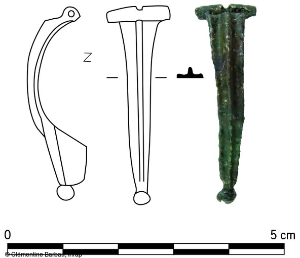 Dessin et photographie de la fibule en alliage cuivreux  mise au jour dans le niveau de la voirie sur le site de Brumath (Bas-Rhin). Fortement corrodée, elle a fait l’objet d’un nettoyage mécanique et chimique et d’un recollage en laboratoire. Il s’agit  d’une fibule dite « d’Aucissa », caractérisée par une charnière formée par le repli de l’arc vers l’extérieur, un porte-ardillon triangulaire plein, un arc rehaussé d’une arête médiane composée d’une ligne perlée et d' un bouton caudal. L’ardillon est néanmoins manquant. Ce type de fibule est particulièrement fréquent au début d