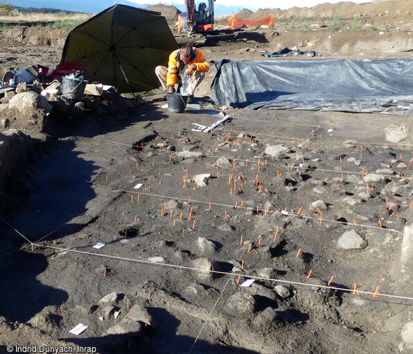 Le niveau du sol du début de l'âge du Bronze ou du Néolithique sur le site de la Carella à Font-Romeu-Odeillo-Via (Pyrénées Orientales) en cours de fouille. Ce reste d'occupation se matérialise par un foyer en cuvette et un sédiment limoneux très sombre, chargé en restes mobiliers (céramiques, industrie lithique taillée, outils de meunerie) mais aussi en charbons et graines. 