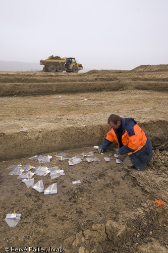 Au premier plan, les structures archéologiques révélées par le décapage sont référencées avant d'être topographiées, fouille du site d'Alizay (Eure), 2011.  Au second plan, on peut se rendre compte du potentiel stratigraphique du site, qui oscille entre 3 et 4m. 