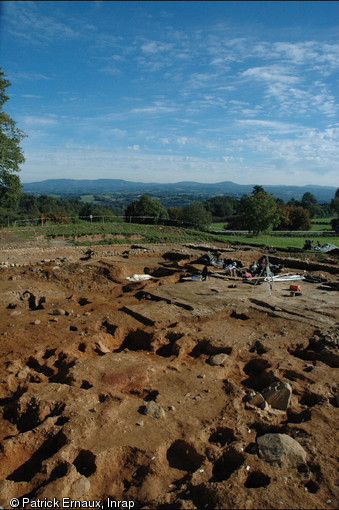 Le site gaulois de Tintignac en Corrèze, avec les empreintes du bâtiment sur poteaux de bois au 1er plan, la fouille du dépot cultuel au second et les Monédière en fond.  